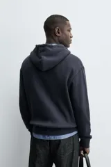 Sudadera hoodie relaxed fit color azul marino, confeccionada en tejido waffle con estructura cuadrillé. Cuenta con capucha ajustable, manga larga, bolsillos delanteros tipo canguro, acabados en rib y cierre frontal de cremallera. Presenta un efecto lavado.