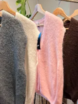 Chaleco tejido de punto en color rosado, con escote en V y cierre frontal mediante botones dorados. Presenta un diseño sin mangas con terminaciones acanaladas en los bordes.