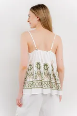 Blusa blanca de algodón liviano con tirantes finos y escote en V. Presenta un corte suelto con pechera fruncida y bordados artesanales en tonos verde y beige con motivos geométricos y florales.