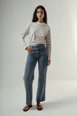 Camiseta de manga larga, cuello redondo, con rayas horizontales marrones sobre fondo blanco. Presenta un pequeño logo bordado en rojo en el pecho.