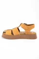 Sandalia tipo guillermina de cuero color camel, con diseño de tiras anchas entrelazadas, cierre con hebilla metálica lateral y suela de plataforma plana en tono marrón.