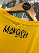 Remera amarilla con estampado de personajes de Naruto en recuadros negros con texto en japonés. El estampado incluye a Naruto, Sasuke, Sakura y Kakashi.