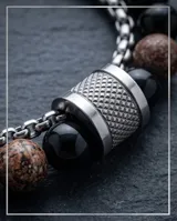 Pulsera doble de acero inoxidable con piedras naturales de ónix negro y piedras jaspeadas en tonos tierra, unidas por un cierre cilíndrico metálico con textura estriada.