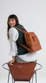 Mochila de diseño clásico en color suela, confeccionada en símil cuero con textura granulada. Presenta un bolsillo frontal con solapa y cierre, compartimento principal con cierre superior, asa de mano y correas regulables para la espalda.