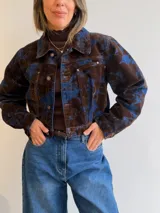 Campera corta de denim con diseño marmolado en tonos azul y marrón, de corte clásico con cierre frontal de botones metálicos y bolsillos en el pecho.