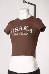 Remera baby tee de morley color chocolate, de calce ajustado al cuerpo y manga corta, con cuello redondo y diseño estampado frontal.