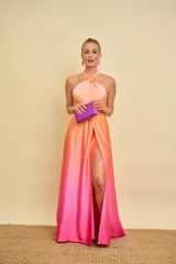 Vestido largo de satén con diseño degradado en tonos salmón y fucsia. Presenta cuello halter con detalle de nudo, falda evasé con tajo frontal pronunciado y espalda descubierta.