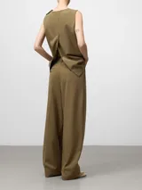 Chaleco sastre de corte recto y diseño minimalista en color verde oliva. Presenta cuello redondo, cierre con dos botones en el hombro izquierdo, sisas amplias y aberturas laterales en el bajo.