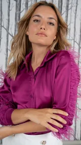 Camisa de manga larga color fucsia, confeccionada en tela satinada, con cuello camisero y puños adornados con plumas fucsia.