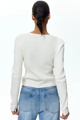 Saco corto en punto acanalado de color blanco, con cuello redondo y tapeta frontal con múltiples botones.