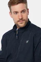 Campera liviana de color verde grisáceo, con cierre frontal, cuello alto y puños elásticos. Presenta un pequeño parche con logo en el pecho.