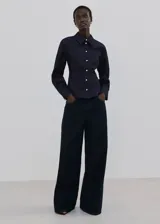 Camisa de denim azul oscuro, con cuello camisero, cierre frontal con botones y mangas largas ajustadas.