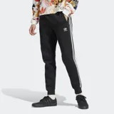 Pantalón de jogging negro Adidas Adicolor con tres rayas blancas a los costados, cintura elástica con cordón de ajuste, bolsillos laterales con cierre y puños acanalados.