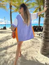 Poncho de playa de tela de toalla, con capucha, mangas cortas y bolsillo canguro. Diseño color block en lila, blanco y naranja.