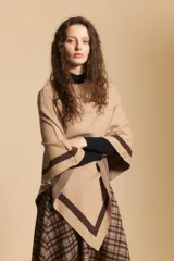 Poncho de silueta amplia y caída fluida, color beige con detalles de líneas en contraste color marrón en los bordes.
