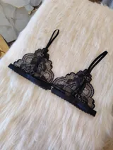 Bralette de encaje negro estilo triángulo, con breteles regulables y cierre frontal con broche de gancho.