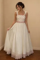 Vestido largo de fiesta con cuerpo tipo corset de tul bordado con motivos florales en tonos rosados y falda amplia de gasa plisada en color crema con borde inferior rosado.