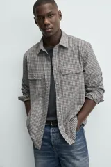 Camisa de corte regular fit confeccionada en tejido de algodón con estampado de cuadros. Presenta cuello solapa, manga larga con puños abotonados, cierre frontal de botones y dos bolsillos de plastrón con solapa en el pecho.