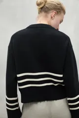 Sweater color crema con rayas horizontales negras en el pecho y los puños, de corte holgado y cuello redondo.