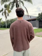 Sweater de punto con diseño bicolor y texturas combinadas, presenta un lado de tejido liso y otro con trenzado vertical. Posee cuello redondo, corte holgado y una etiqueta decorativa en el frente.