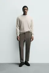 Pantalón de corte slim fit y color negro, confeccionado en tejido elástico. Cuenta con cintura elástica, trabillas, bolsillos frontales y cierre con cremallera y botón.