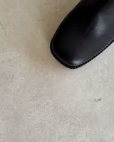 Botín corto de cuero color marrón oscuro, con punta cuadrada y taco ancho acanalado.