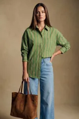Camisa de corte oversize con estampado de rayas verticales en tonos verde, blanco y ocre. Presenta cuello clásico, cierre frontal con botones, bolsillo en el pecho y mangas largas con puños abotonados.