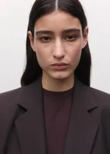 Blazer de corte sastre y diseño cruzado, con cierre de botones frontales, solapas clásicas y bolsillos laterales con solapa. Presenta una estructura entallada y hombros definidos.