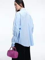 Camisa de corte oversize color celeste, con cuello clásico, cierre frontal de botones y detalle de apliques brillantes en la parte delantera.