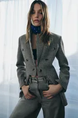 Blazer Zara de corte asimétrico confeccionado en tejido con lana. Presenta un diseño de cuadros, cuello con solapas de muesca, manga larga y cierre frontal cruzado con botones. El bajo es asimétrico con una abertura pronunciada en la espalda y cuenta con forro interior.
