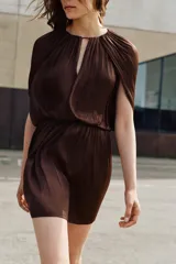 Vestido corto de tejido satinado color marrón, con cuello redondo, mangas largas con diseño fluido y cintura elástica. Presenta una abertura frontal y cierre posterior con botón.