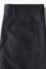 Pantalón de traje negro, de corte regular fit y silueta clásica, con bolsillos laterales y traseros ribeteados, cierre con cremallera y botón oculto.