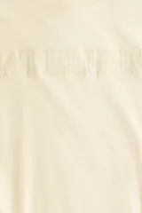 Remera oversized de punto de algodón color amarillo claro, con cuello redondo, mangas cortas y hombros caídos. Cuenta con la palabra "ATELIER" bordada en relieve en el frente.