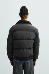 Cazadora acolchada de hombre con acabado engomado, cuello subido con interior de borreguillo, cierre frontal de cremallera, bolsillos laterales con cremallera y puños y bajo elásticos.