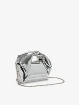 Bolso de hombro plateado con forma rectangular y efecto arrugado. Tiene asa superior con nudo y logo grabado en el frente.