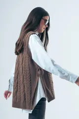 Chaleco de punto color marrón con diseño de ochos, cuello redondo y lazos laterales ajustables.