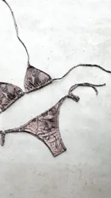 Bikini color dorado brillante, con corpiño triangular de atar al cuello y espalda, con almohadillas desmontables. La bombacha es vedetina con tiras ajustables a los costados.