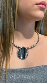 Gargantilla rígida de metal plateado con diseño minimalista que presenta un dije circular central con acabado espejado.