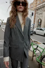 Blazer recta gris con hombreras, cuello solapa, manga larga, bolsillos delanteros con solapa y cierre frontal con un botón.