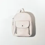 Mochila pequeña de cuero sintético color blanco con bolsillo frontal con broche imantado y dos bolsillos laterales con cierre.