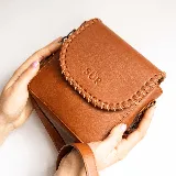 Mini cartera bandolera de cuero, de formato compacto y diseño atemporal con solapa frontal y costuras artesanales decorativas en el borde. Cuenta con el logotipo de la marca grabado en la parte delantera y correa larga regulable.