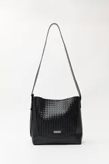 Cartera de hombro color negro con diseño trenzado en el panel frontal y laterales lisos. Cuenta con una correa larga ajustable y una placa metálica pequeña con el logo de la marca en la parte inferior.