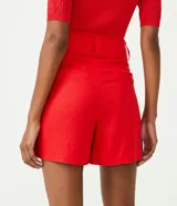 Short rojo de lino con cintura alta, cinturón con hebilla cuadrada forrada, pliegues delanteros y dos bolsillos laterales.