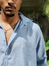 Camisa de lino rayada en tonos celeste y blanco, con cuello y botones frontales. Presenta un estampado en el frente y la espalda.