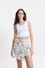 Falda corta tipo pareo con diseño anudado frontal que genera un efecto envolvente. Presenta un estampado marmolado en tonos neutros y cálidos.