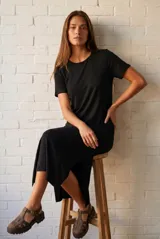 Vestido midi de color negro, con cuello redondo y mangas cortas. Presenta un corte recto con aberturas laterales en el ruedo, confeccionado en un tejido suave y liviano con caída fluida.