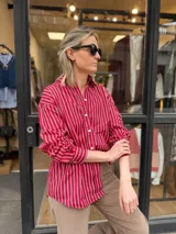 Camisa oversize con diseño de rayas verticales rojas y blancas, de manga larga con puños abotonados y cierre frontal con botones.