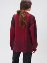 Cardigan oversize de tejido de punto grueso con diseño de bloques de color en tonos beige y marrón. Presenta cuello en V, cierre frontal con botones, mangas largas abullonadas y parches decorativos en el pecho y el hombro.