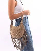 Bolso de hombro estilo boho confeccionado en gamuza color bordó. Presenta un diseño semicircular decorado con tachas metálicas plateadas dispuestas en líneas curvas y flecos largos en todo el borde inferior. Cuenta con cierre superior y correa ajustable para llevar al hombro.