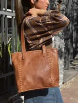 Cartera tipo tote de cuero color camel, con diseño estructurado, costuras decorativas laterales y doble asa superior para el hombro.